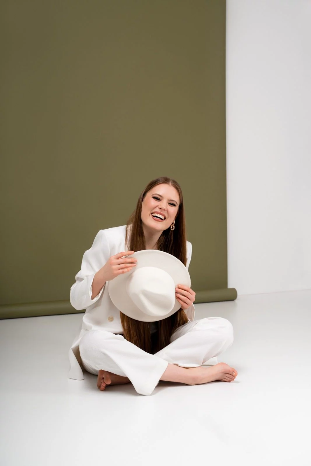 Portretna fotografija rdečelaske deklice z belimi hlačami, ki se nasmeja in gleda v daljavo, posneta v našem fotografskem studiu v Ljubljani.