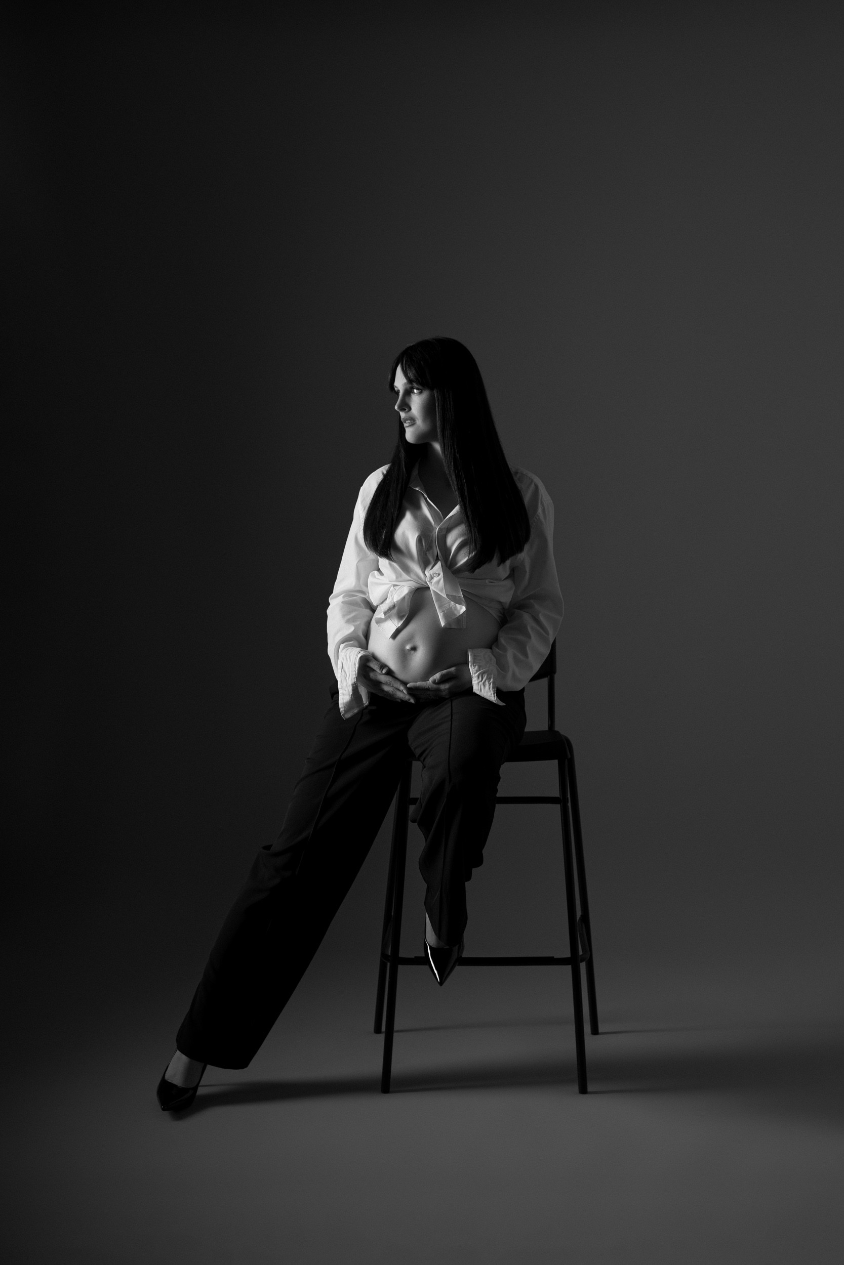 Noseča ženska na črnem stolu v foto studiu