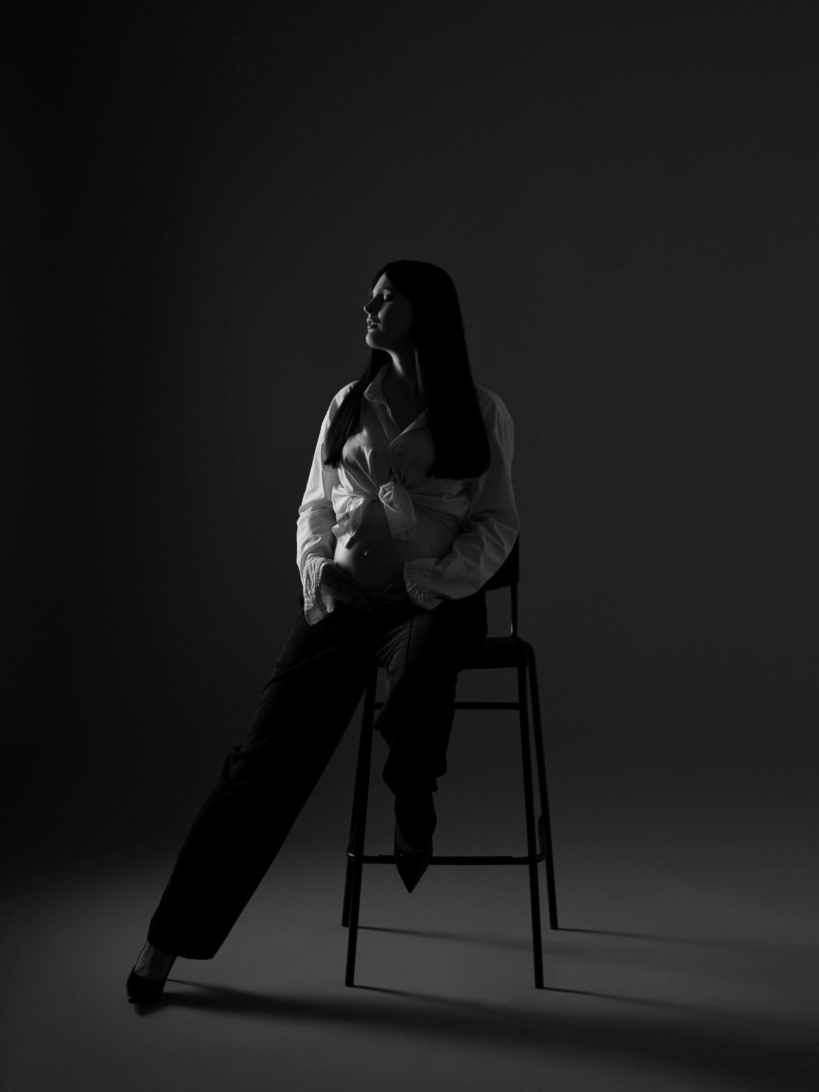 Noseča ženska na črnem stolu v foto studiu