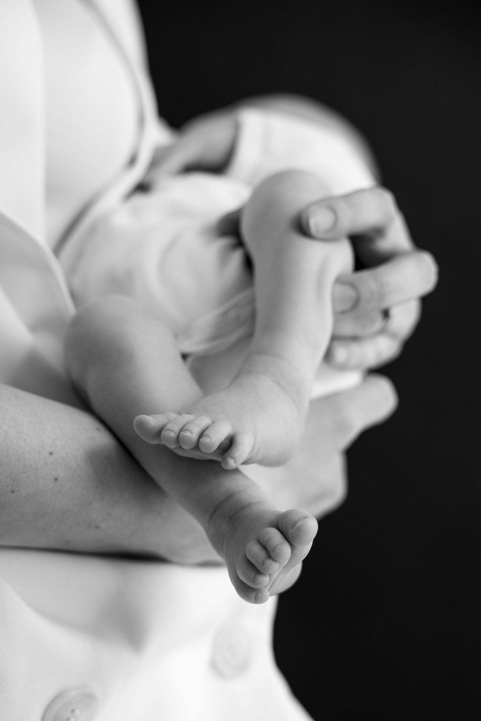 Nogice novorojenčka med fotografiranjem v studiu. Mama drži novorojenčka na rokah