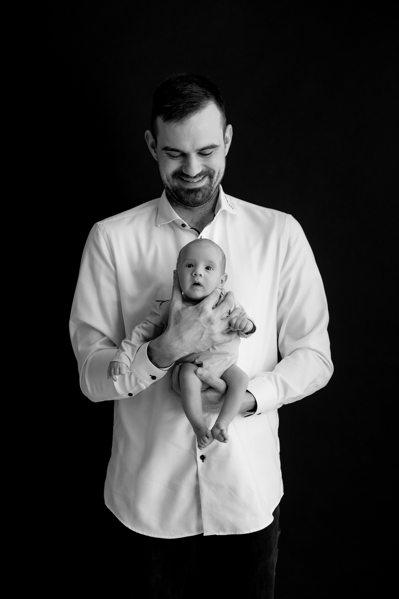 Črno-bela fotografija, ki prikazuje očeta, ki drži novorojenčka